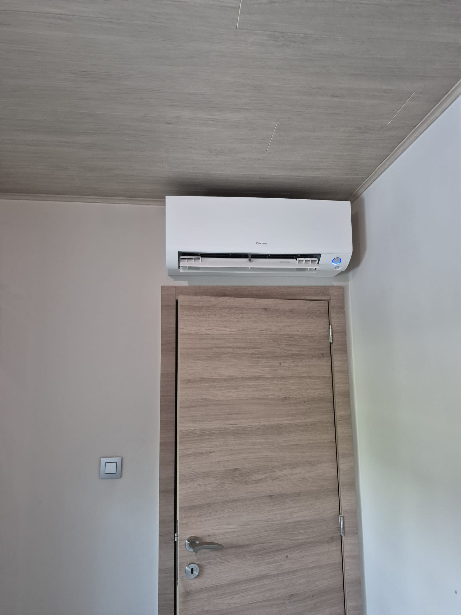 Dezelfde binnenmuur met een geplaatste Daikin-airco boven de houten deur